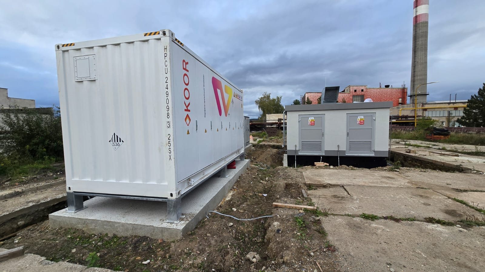 Kontejner bateriového úložiště KOOR na betonovém základu, v pozadí trafostanice